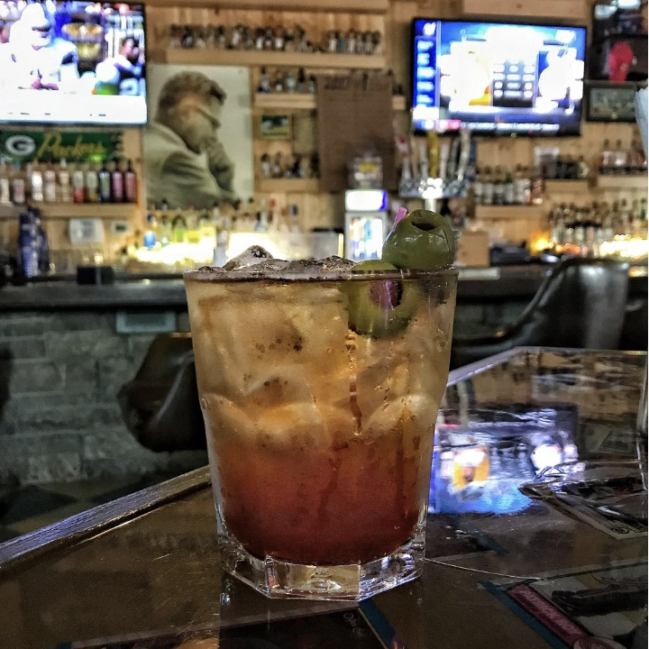 A brandy Old Fashioned on a table in a bar with TVs showing football.