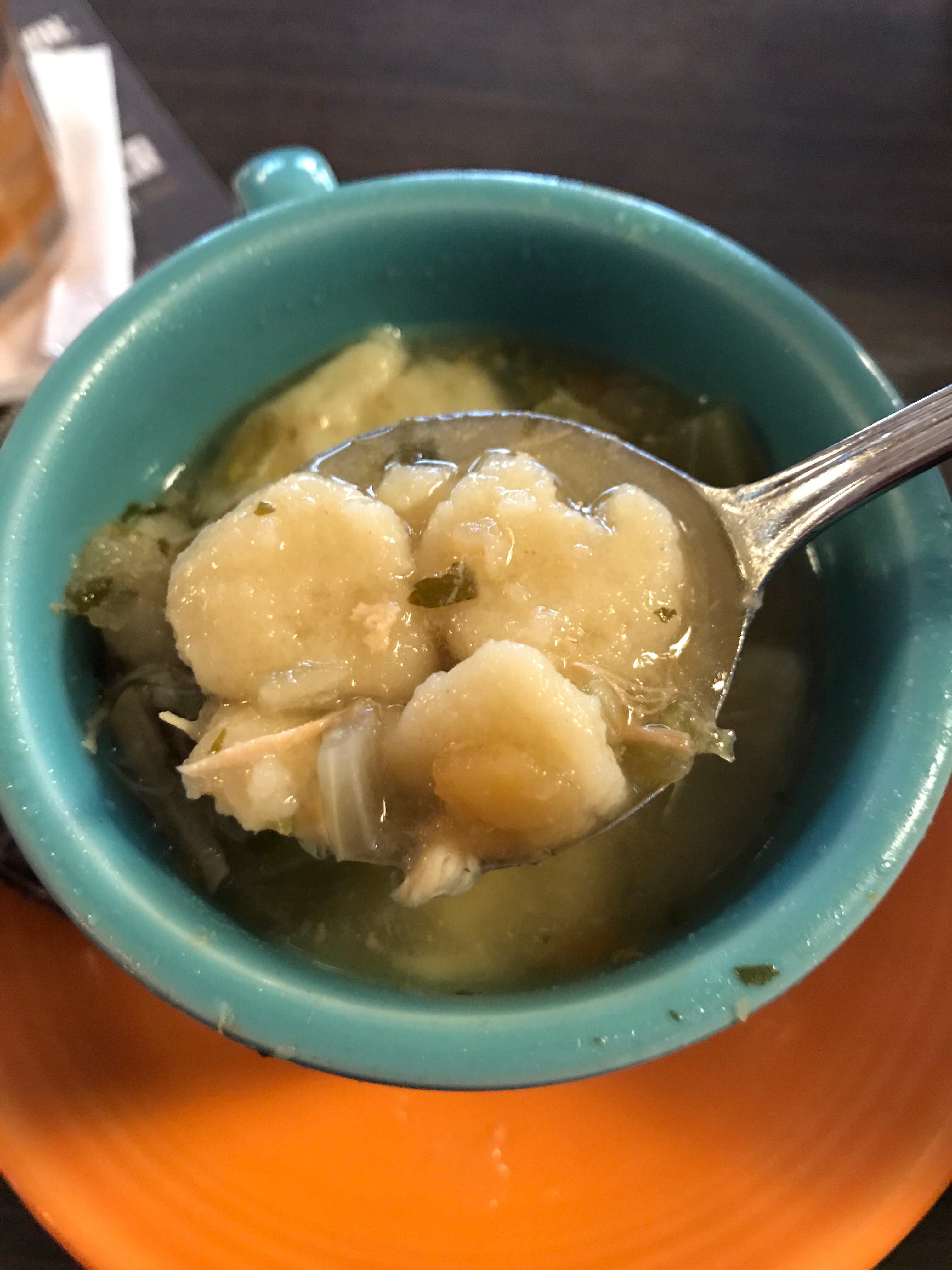A spoon of chicken and dumpling soup held above a blue bowl of the same.