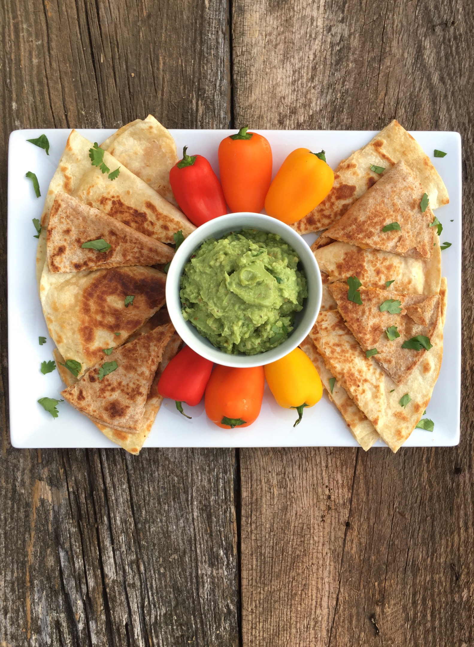 Slices of quesadillas surrounding peppers and a cup of guacamole. 