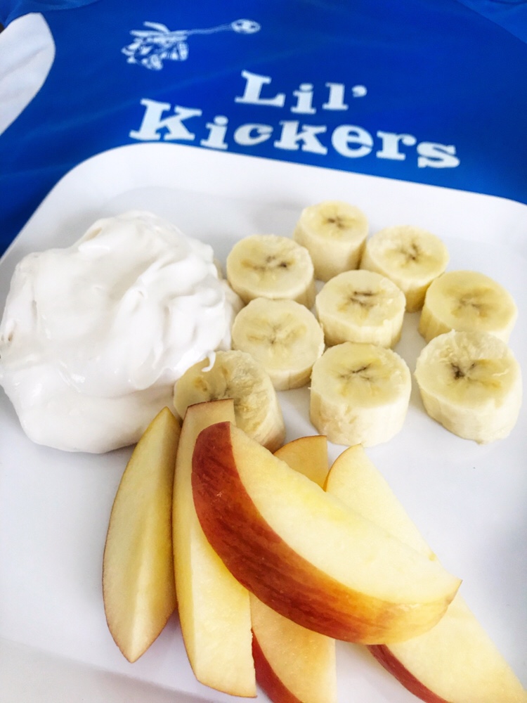 A plate of sliced bananas, apple, and whipped yogurt on a Lil' Kickers jersey.