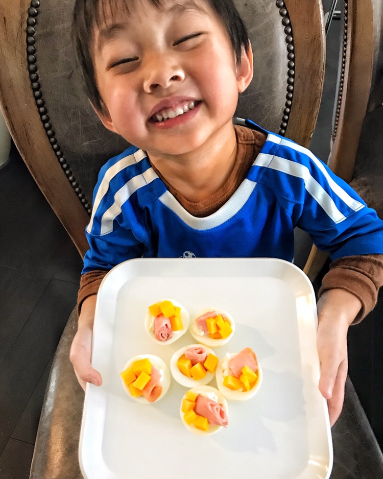 A child smiling and holding a plate of ham and cheese egg white cups.