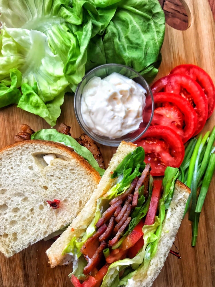 The completed BLT alongside the ingredients inside it spread out on a cutting board.