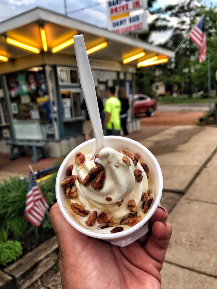A cup of ice cream with walnuts and a plastic spoon being held in front of Dari Maid.