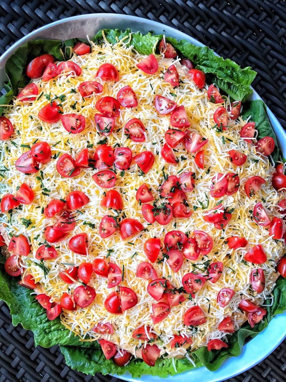 A big bowl of taco dip with shredded cheese and chopped tomatoes.
