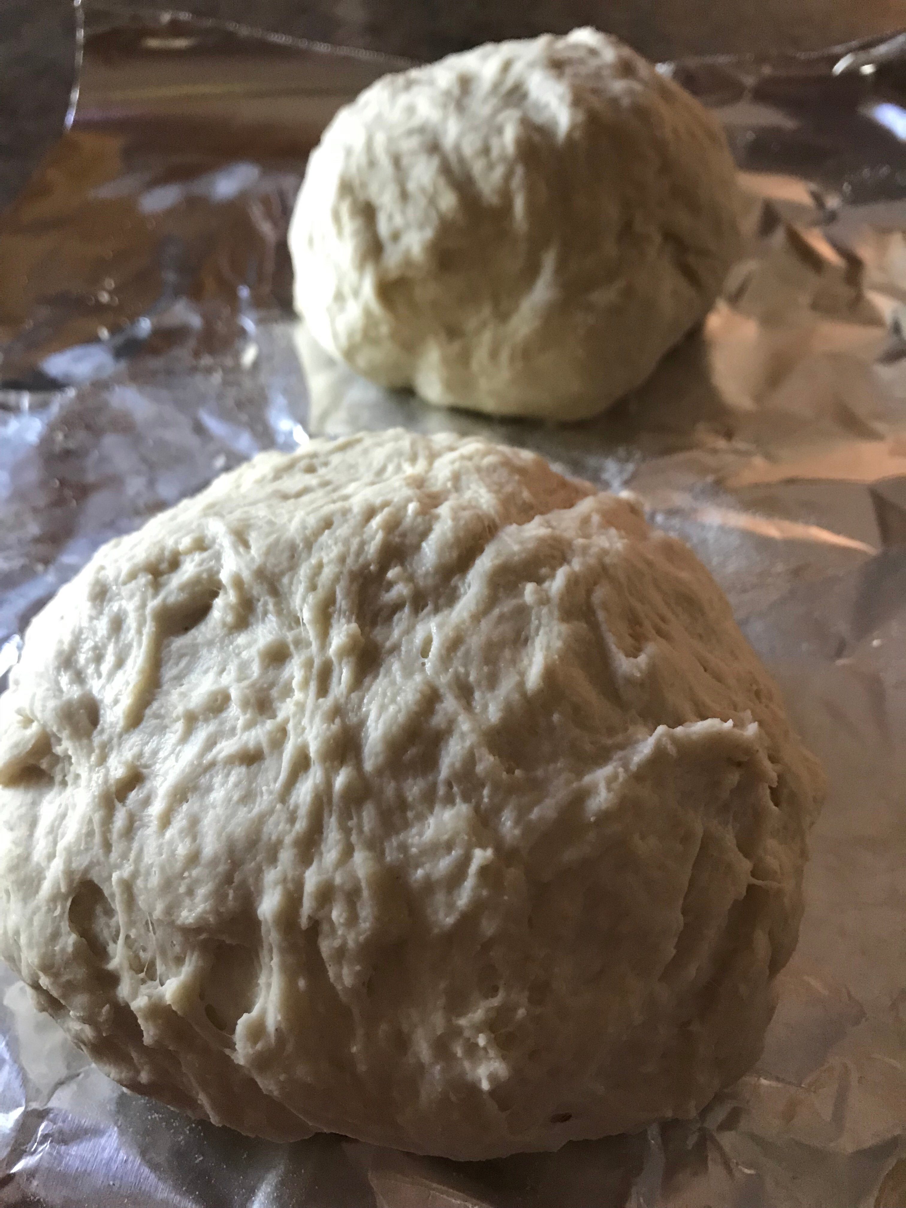Two balls of pizza dough on aluminum foil.