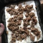 Sausage crumbles on raw pizza dough in a square tin.