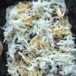 Sausage crumbles, shredded cheese, and mushroom on raw pizza dough in a square tin.