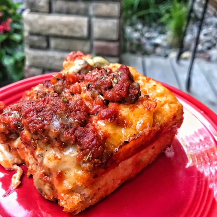A close up slice of Detroit pizza on a red pate. 