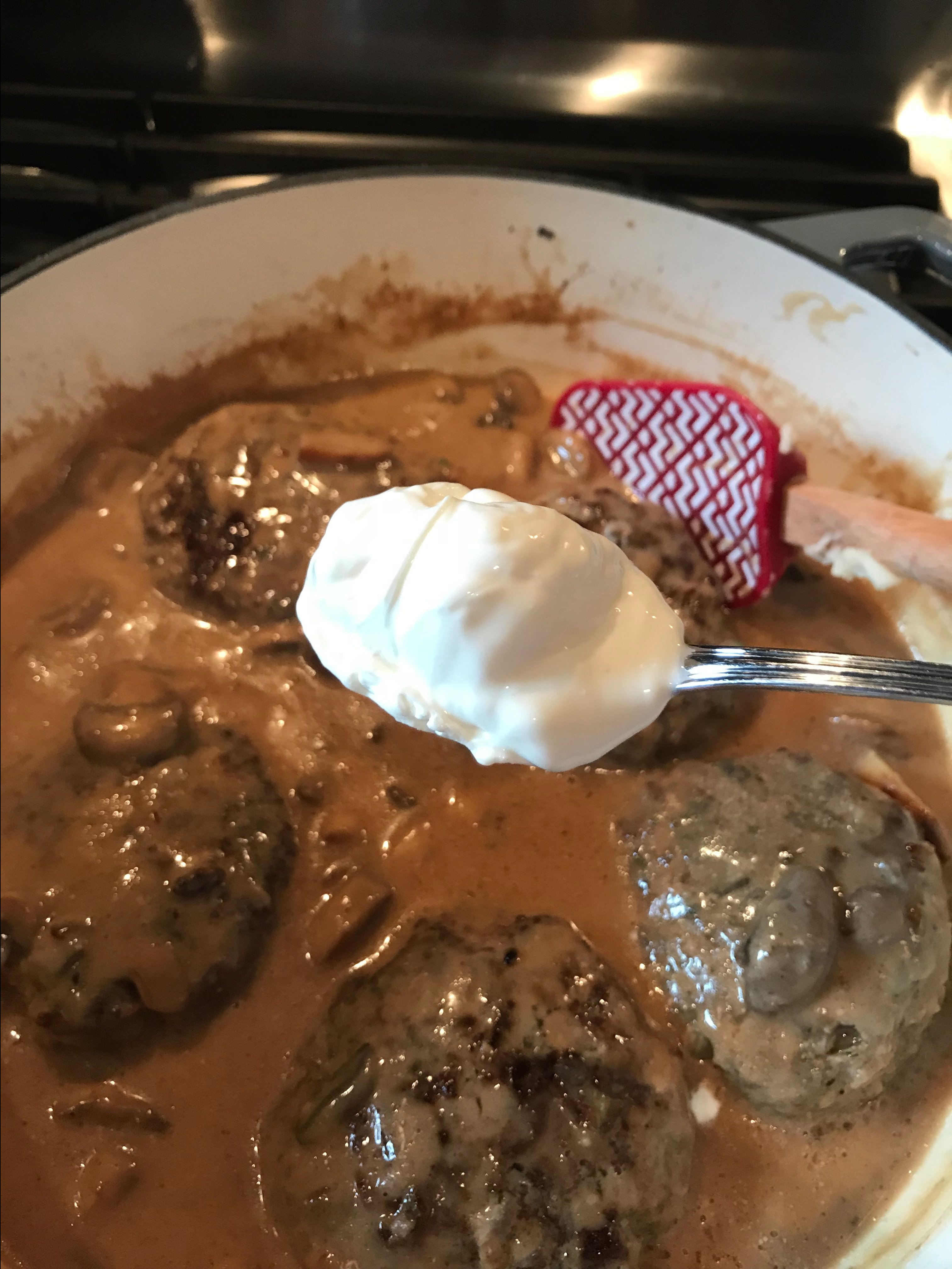 A spoon of sour cream about to be put in the cooking burgers