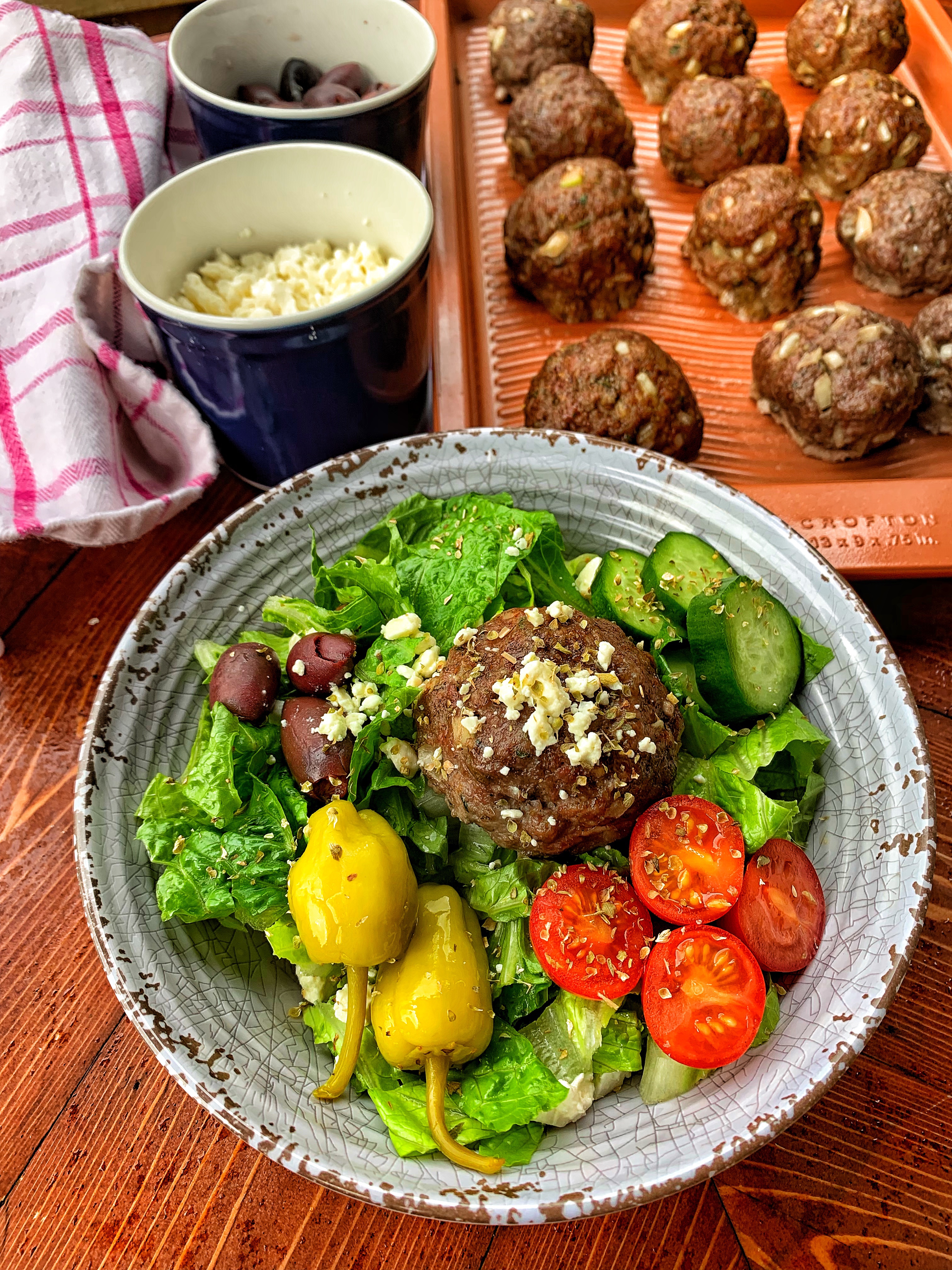 Greek salad topped with a gyro meatball next to a tray of more meatballs
