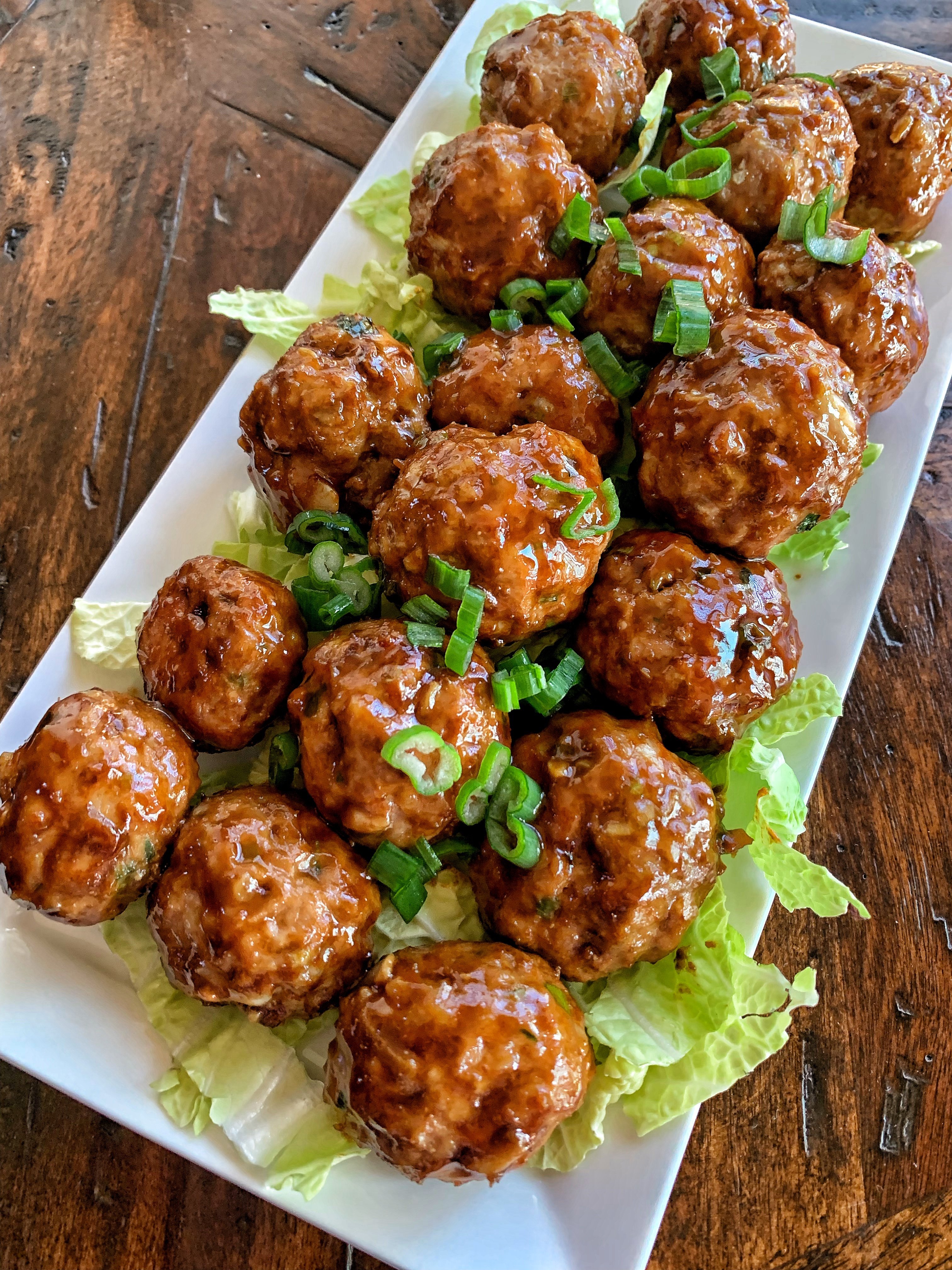 Overhead shot of meatballs made with pork and peanuts on a white plate with green onions and a glaze.