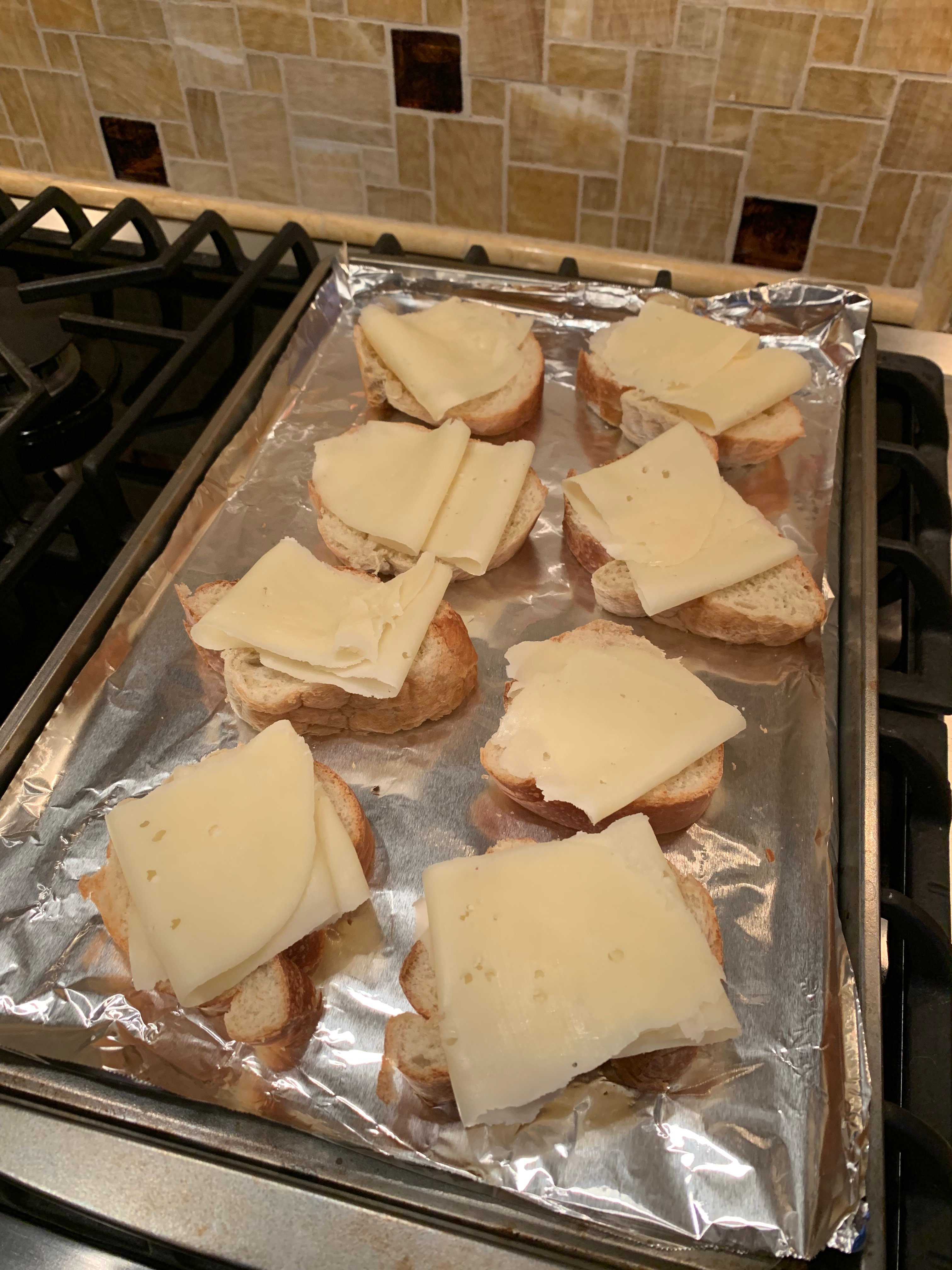 French bread slices with slices of Swiss cheese folded on top sitting on a sheet pan covered with foil.