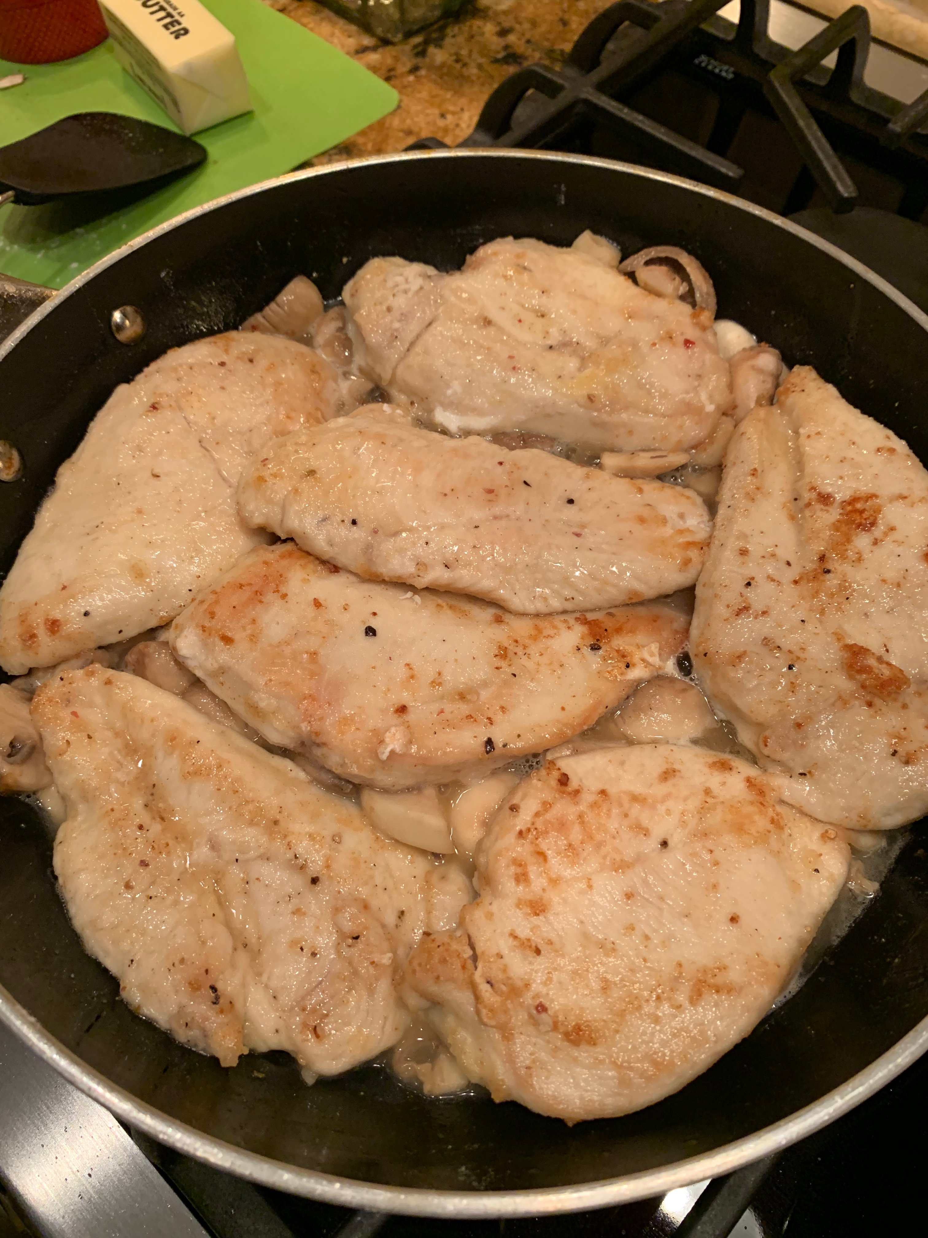 Skillet with chicken breasts and mushrooms and white wine sauce cooking on the stove