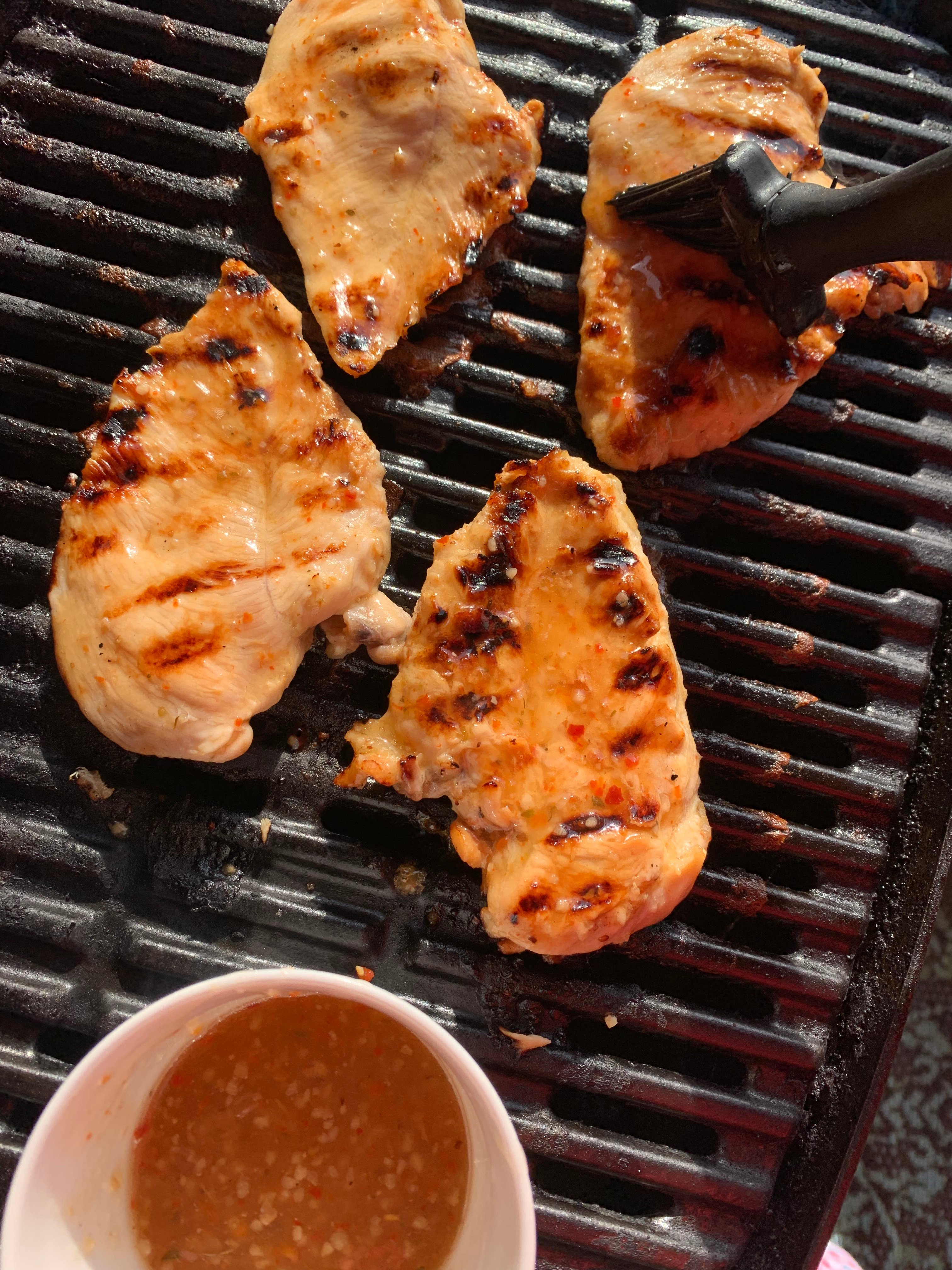 4 Chicken breasts on a weber grill being basted with Italian dressing.