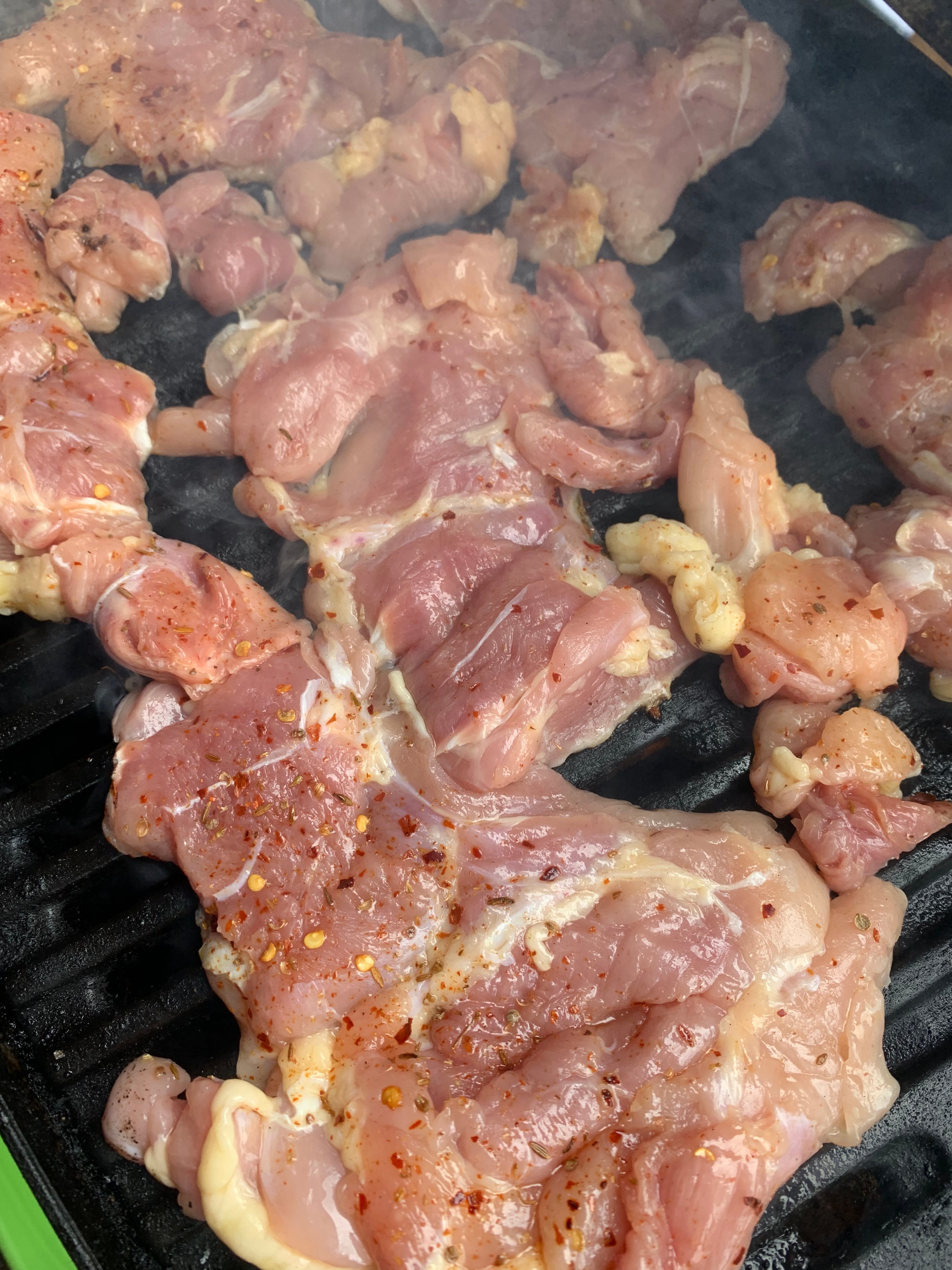 Chicken thighs seasoned with red pepper and salt and olive oil on the grill.