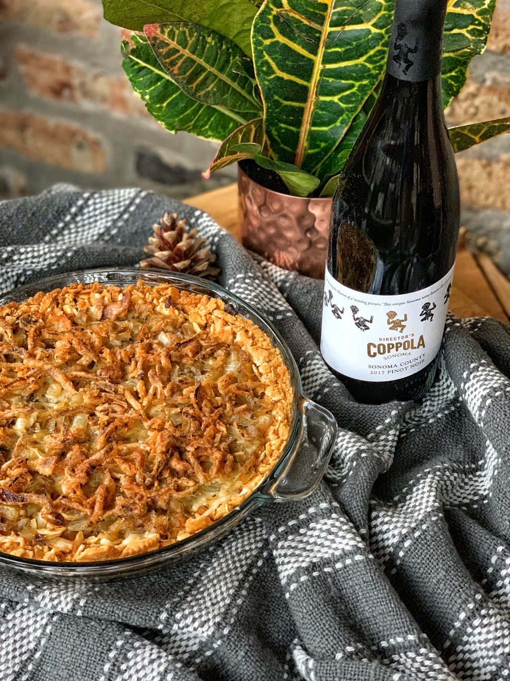Creamy onions, white cheddar cheese and crispy onions in a casserole next to a bottle of Coppola Pinot Noir wine.