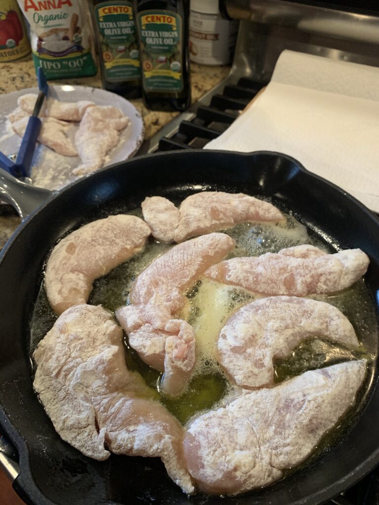 The floured chicken cooking in the pan