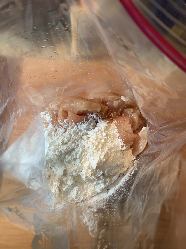 Chicken pieces being tossed in corn starch in a Ziploc bag