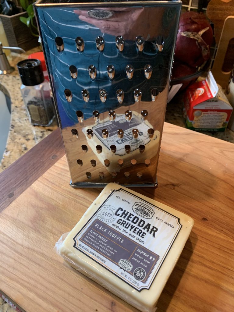 A block of Cheddar Gruyere black truffle cheese next to a cheese grater