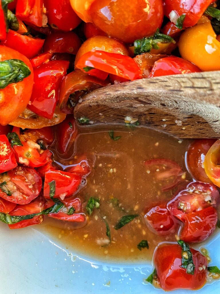 The tomatoes combined with the salt being stirred with a wooden spoon
