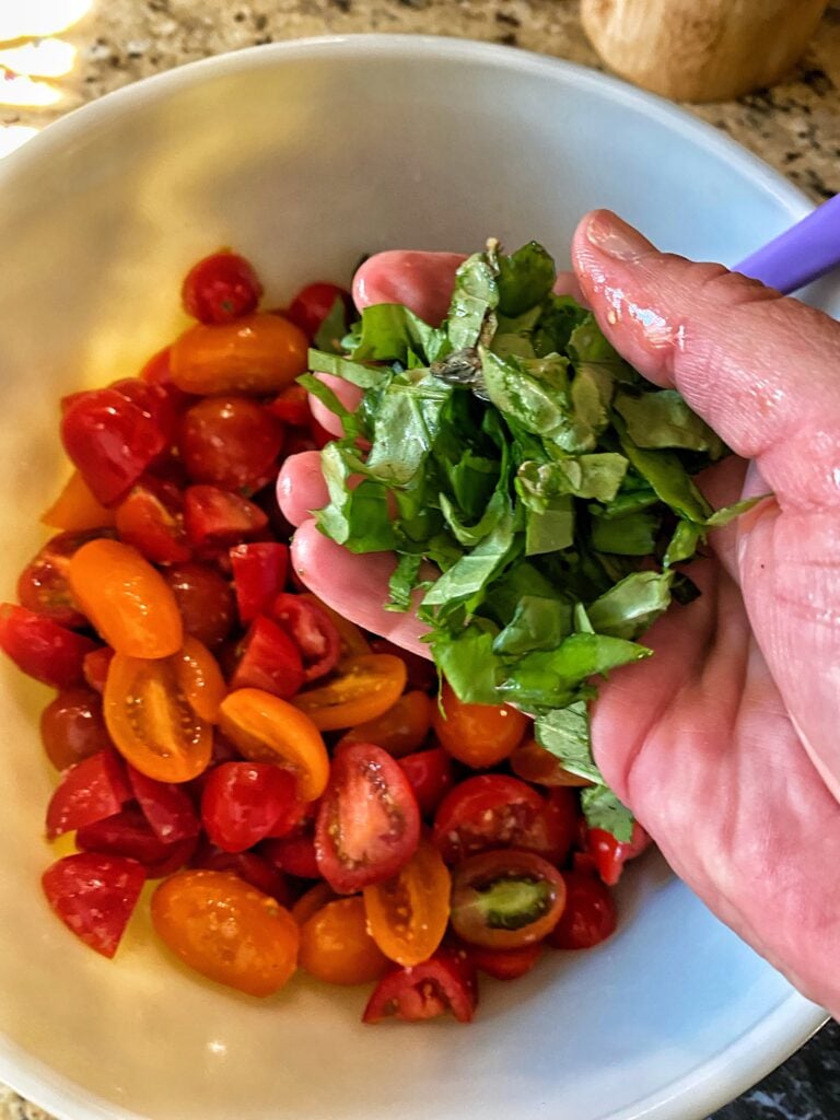 Ripped basil being held over cut up tomatoes