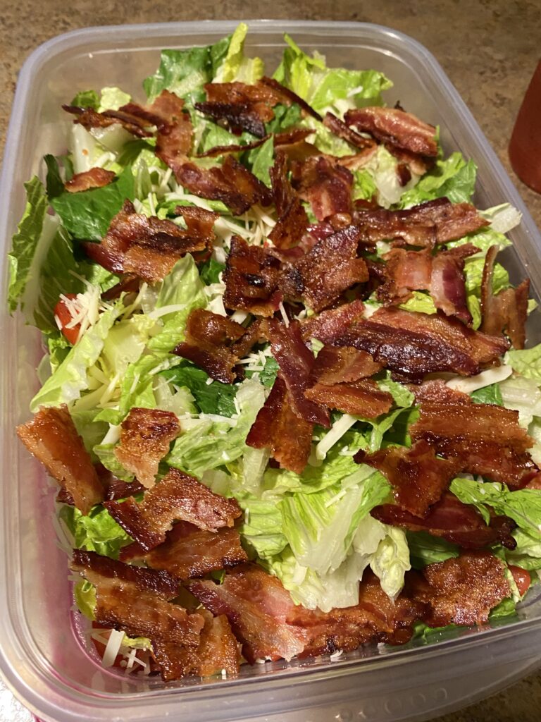 Salad topped with bacon in a plastic container