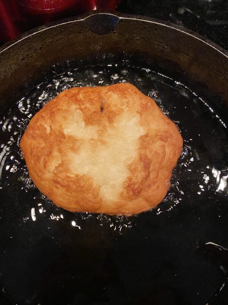 A biscuit pulled into tack shape, frying in a pan