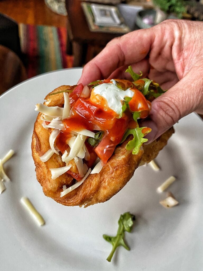 A puffy chicken taco with cheese, sour cream, and hot sauce