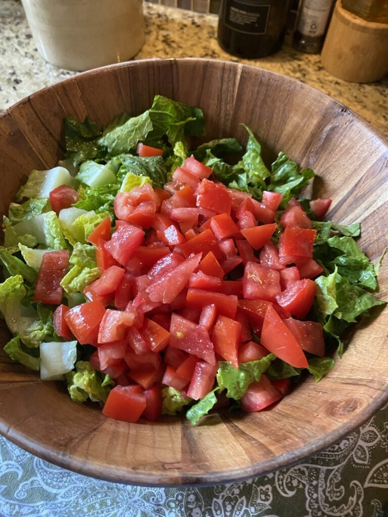 Diced tomatoes on chopped lettuce in a wooden bowl