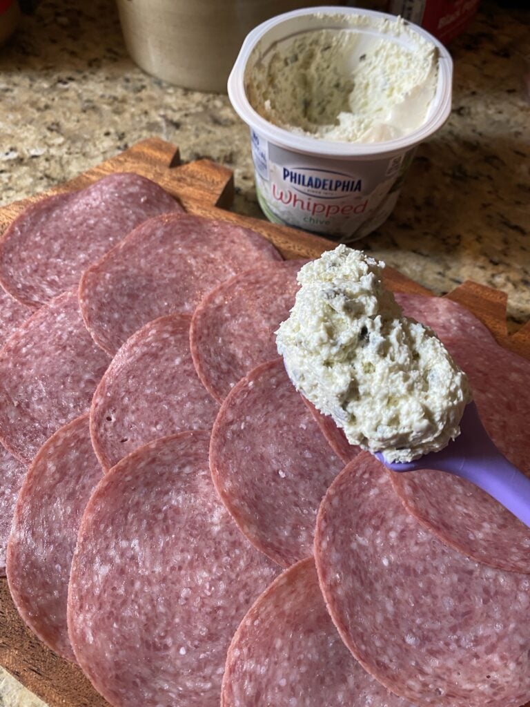 Cream cheese about to be spread on the slices of salami