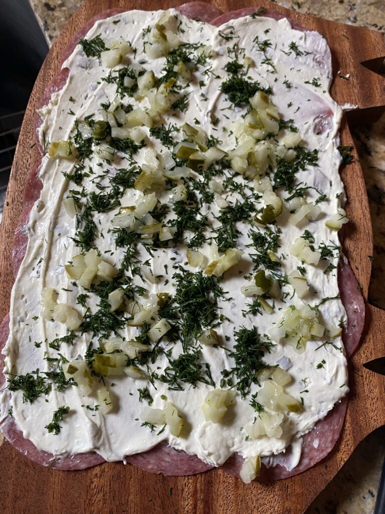 The layered salami covered with cream cheese, chopped pickle, and herbs