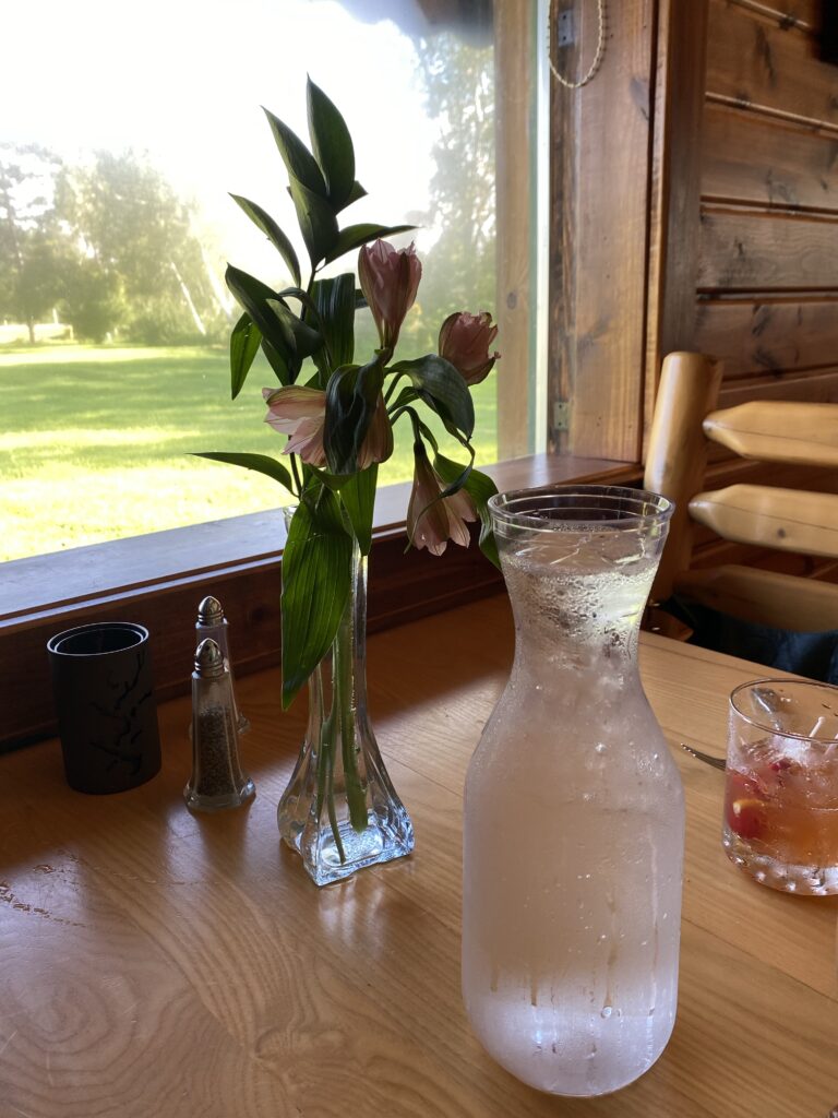 A table by the window with water and flowers in a vase