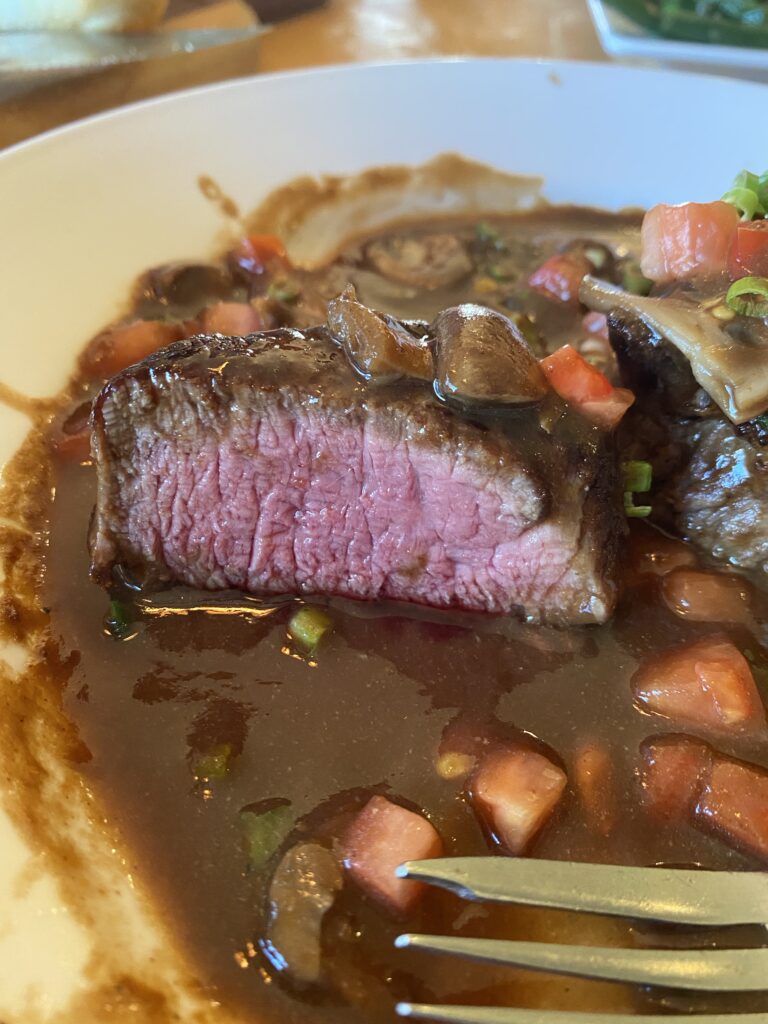 A piece of steak covered in mushrooms, carrots, and gravy cut open to show the medium rare interior