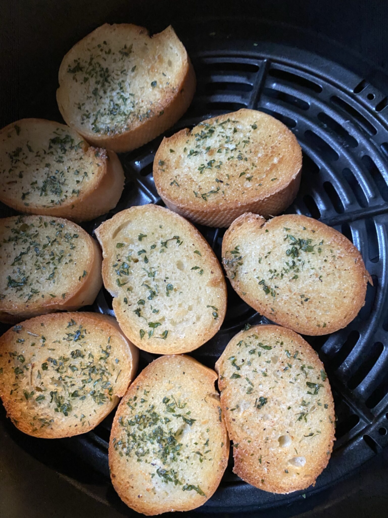 Buttered French bread slices seasoned with garlic powder and parsley inside an air fryer basket.