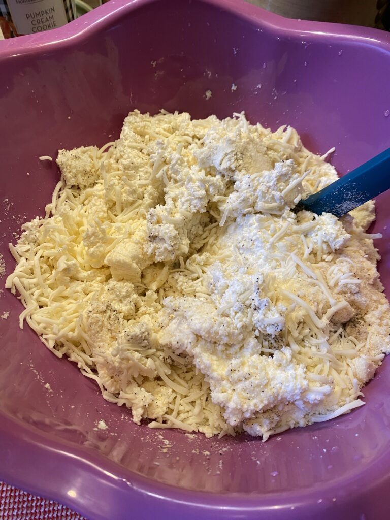 Shredded cheese and ricotta with seasoning in a purple bowl
