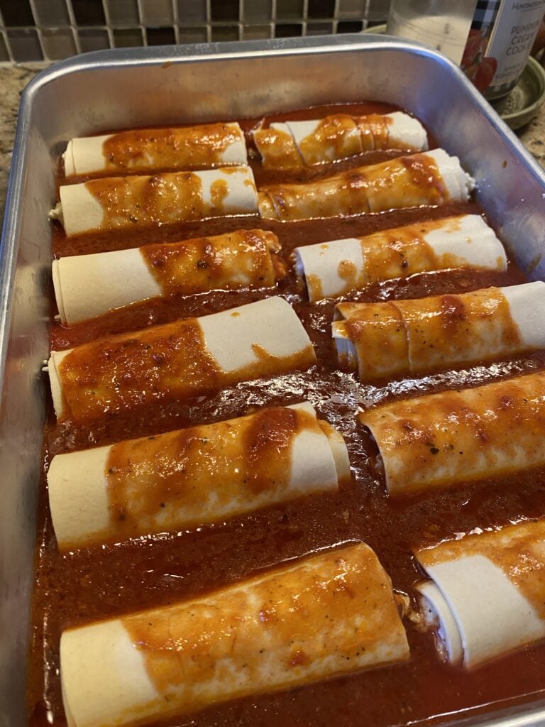 Wrapped manicotti topped with sauce before being baked