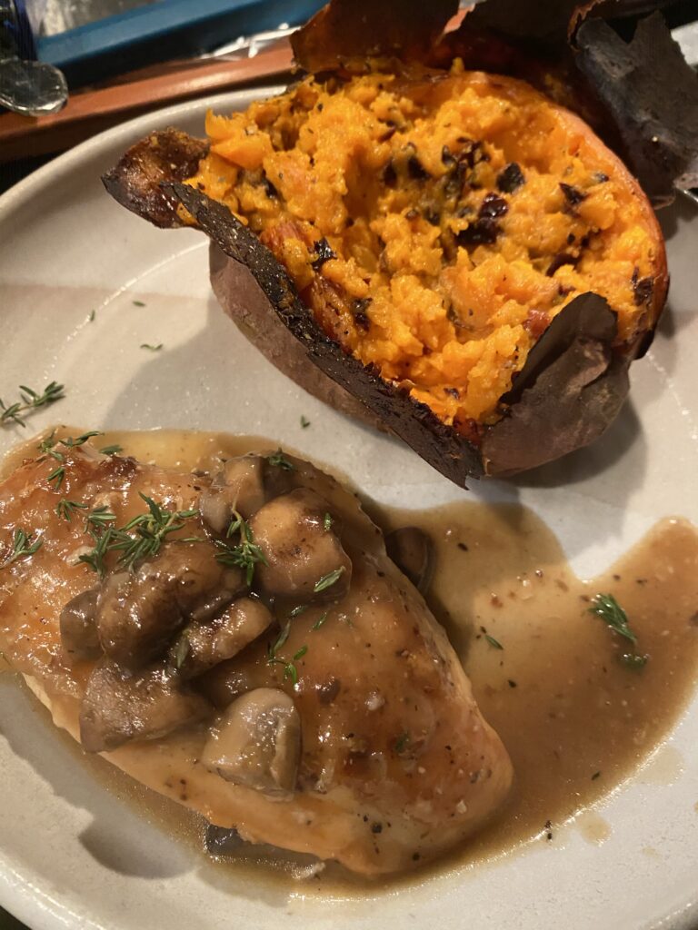 Skillet chicken with mushroom sauce on a plate with an open roasted sweet potato