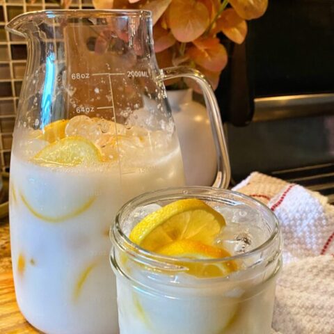 A glass pitcher of creamy lemonade with fresh lemon slices.