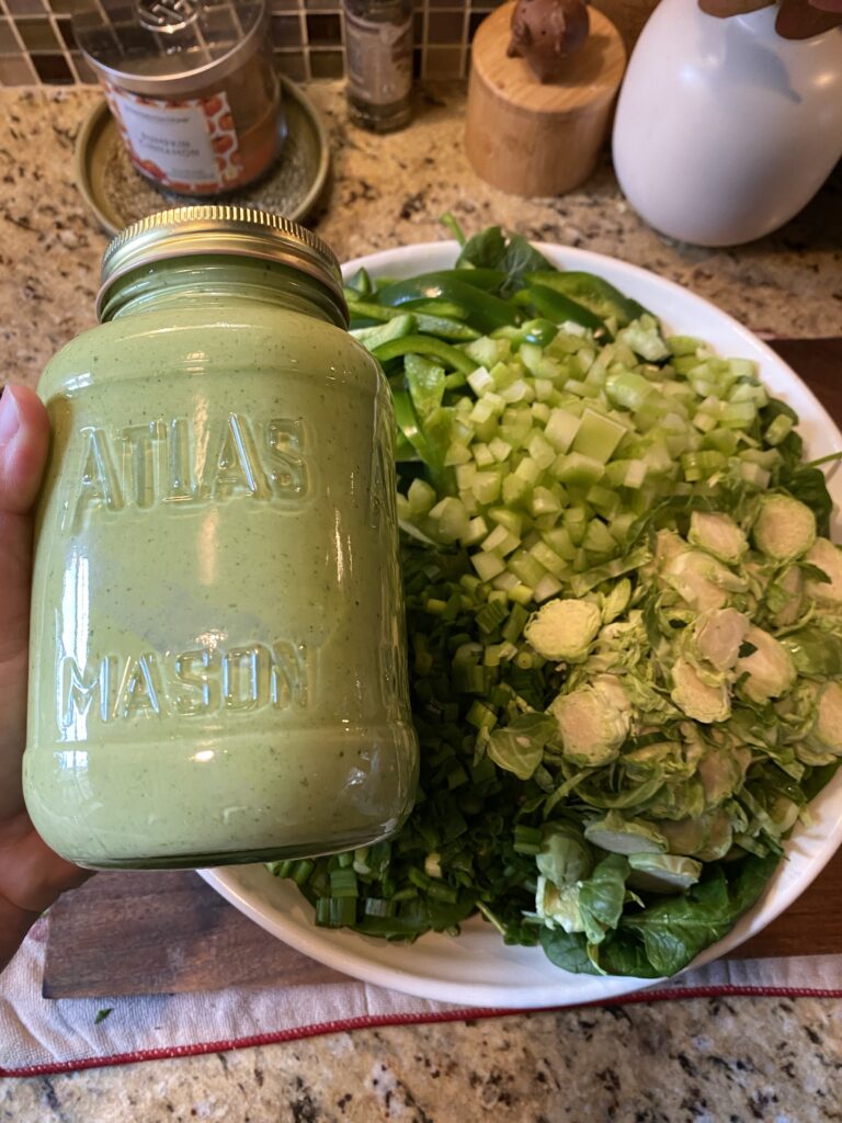 A big bowl of green salad with a jar of green dressing