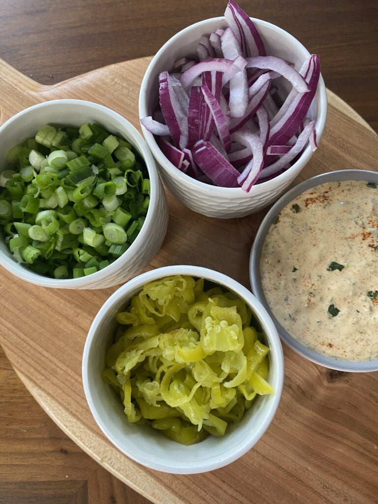 The toppings for the Mardi Gras sandwich including green onions, banana peppers, sauce, and red onion