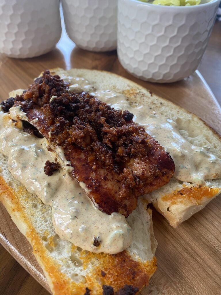 A sausage sliced open with chorizo on top on a hoagie roll with sauce spread on it