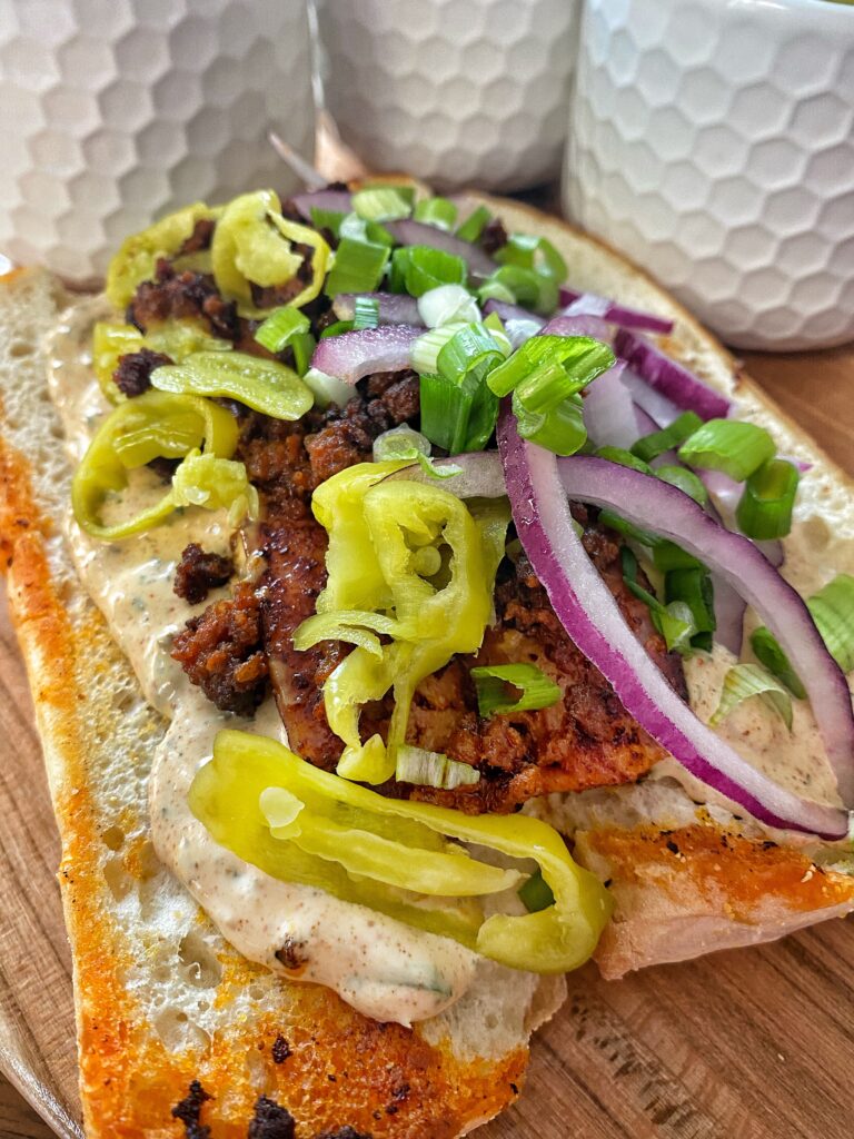 A close up of the Mardi Gras sausage sandwich featuring onion and banana peppers