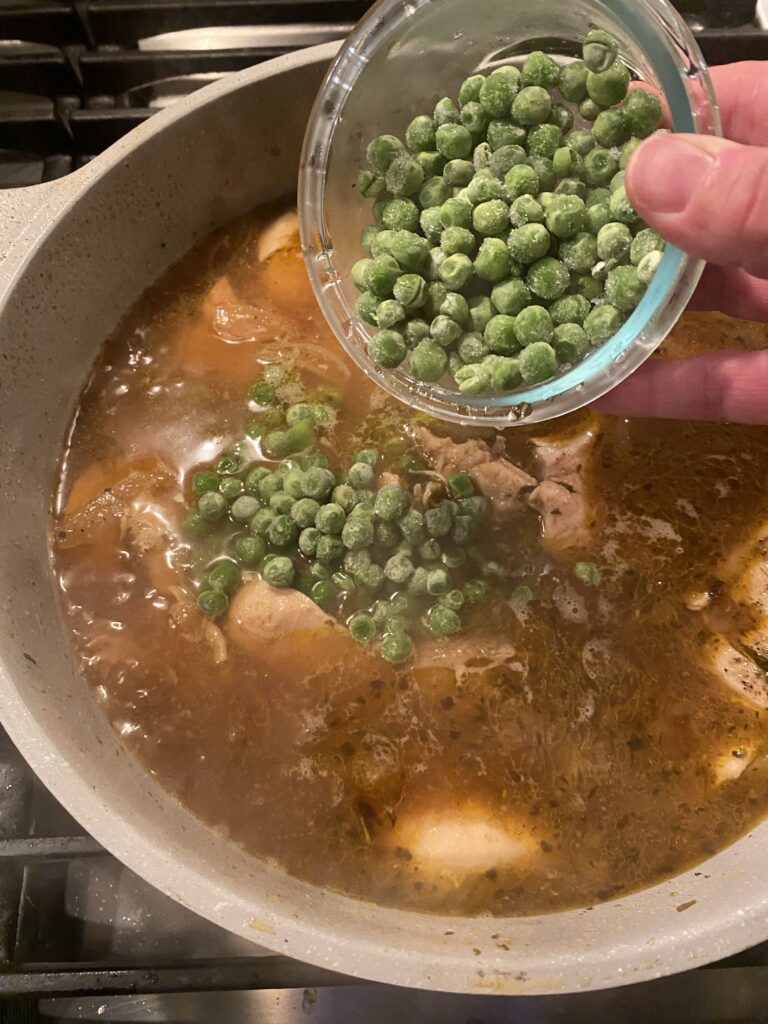 Frozen peas being poured into the chicken mixture in the pot