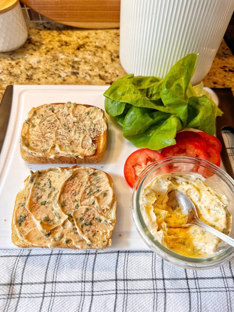 Two slices of bread with sauce spread on them next to lettuce and tomato