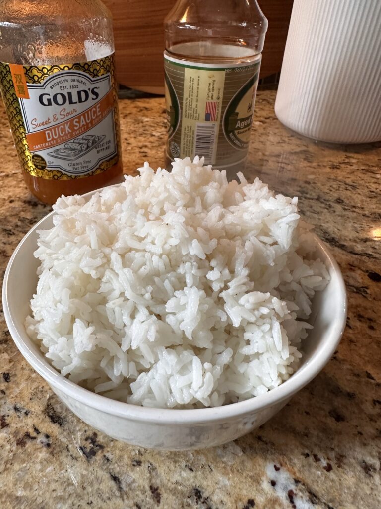 A bowl of white rice in front of a bottle of duck sauce