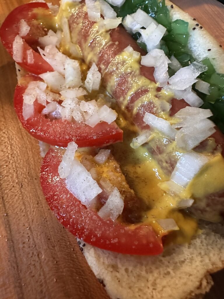 A close up of the hot dog with mustard, tomato, onions, and relish