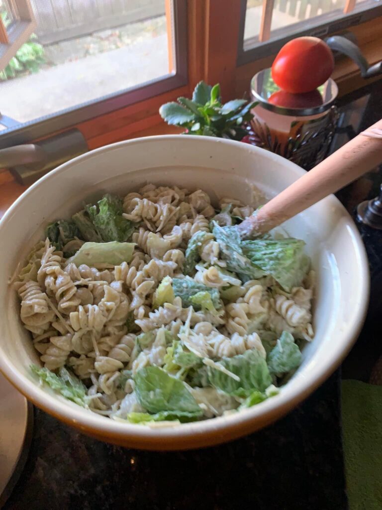 Caesar pasta salad in a bowl with a wooden spoon