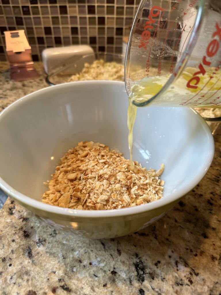 Melted butter being poured into a bowl of crushed Ritz crackers