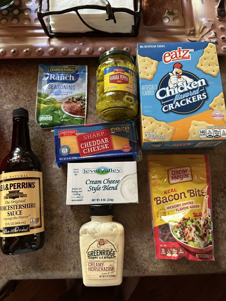 The components for the supper club cheeseball, including Worcestershire sauce, creamy horseradish, bacon bits, chicken flavored crackers, sharp cheddar cheese, cream cheese, banana peppers, and ranch seasoning