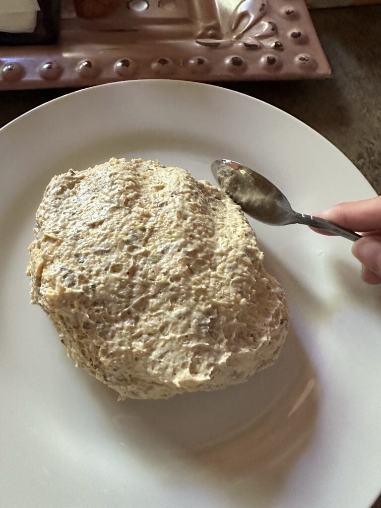 The cheeseball being molded into shape with a spoon